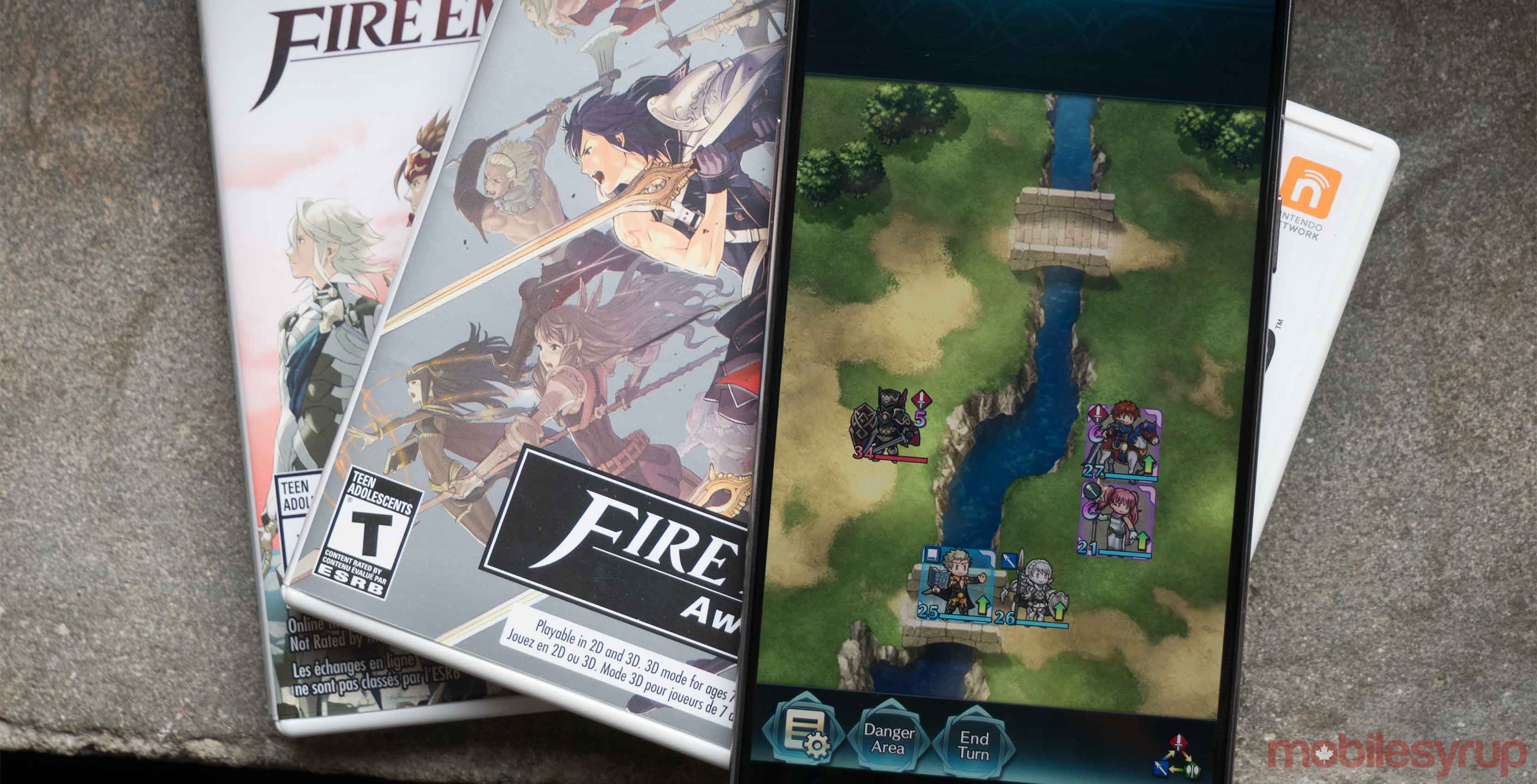 Fire Emblem Heroes playing on a phone that is laying on top of video game cases
