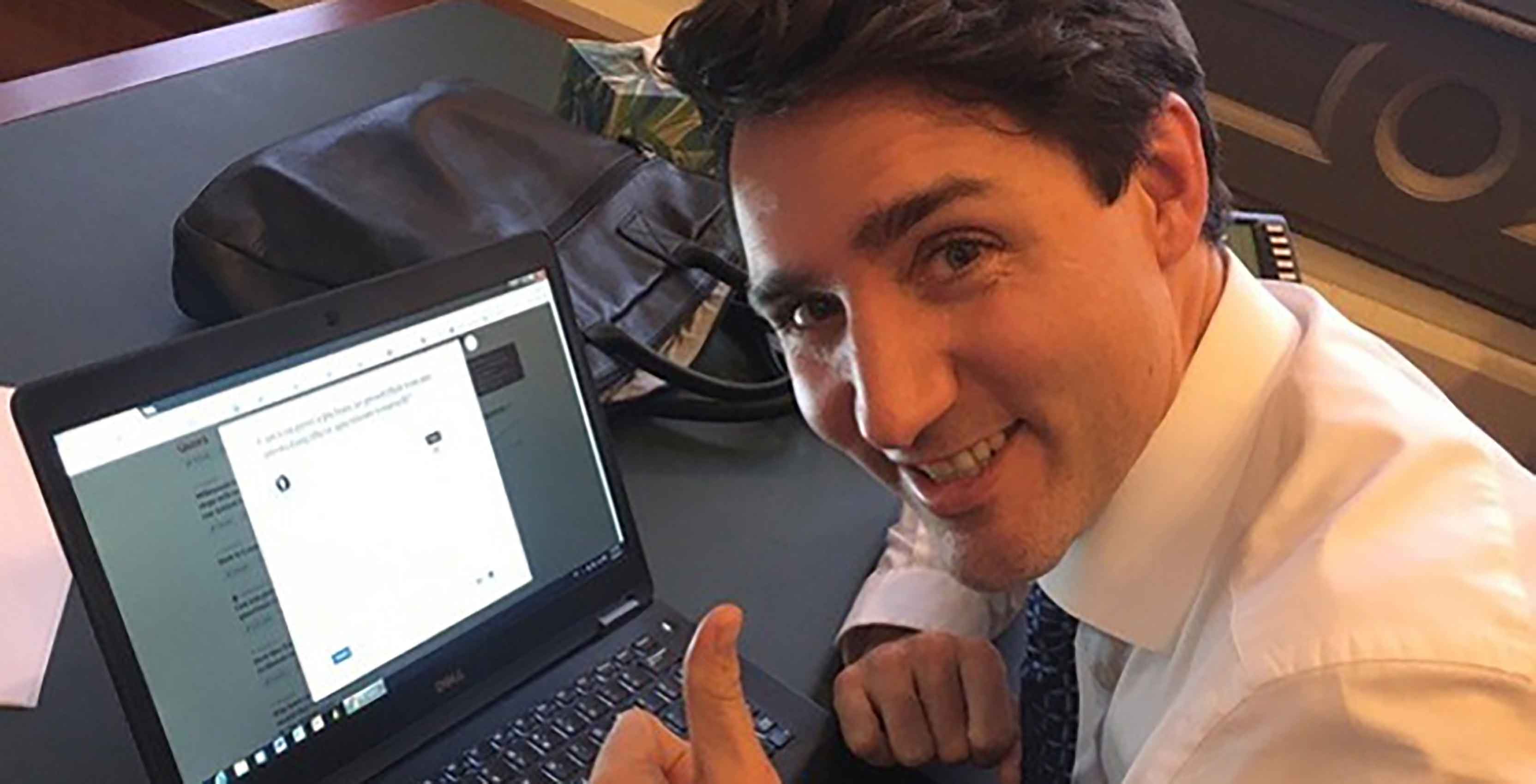 trudeau with his thumbs up beside a laptop.