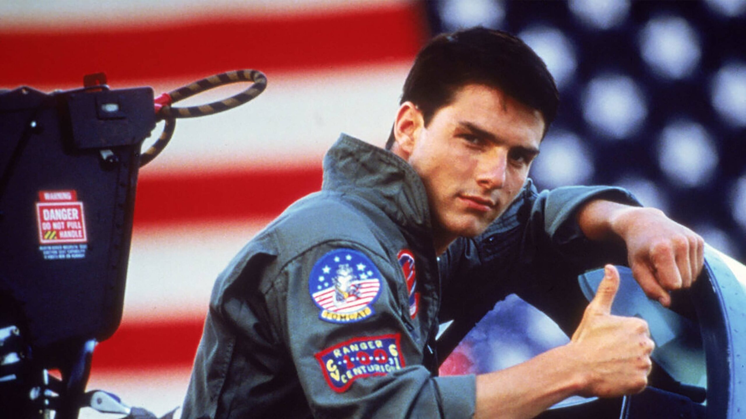 An image from 1986's Top Gun. Tom Cruise as Pete "Maverick" Mitchell is giving a thumbs up from the cockpit of a ship.