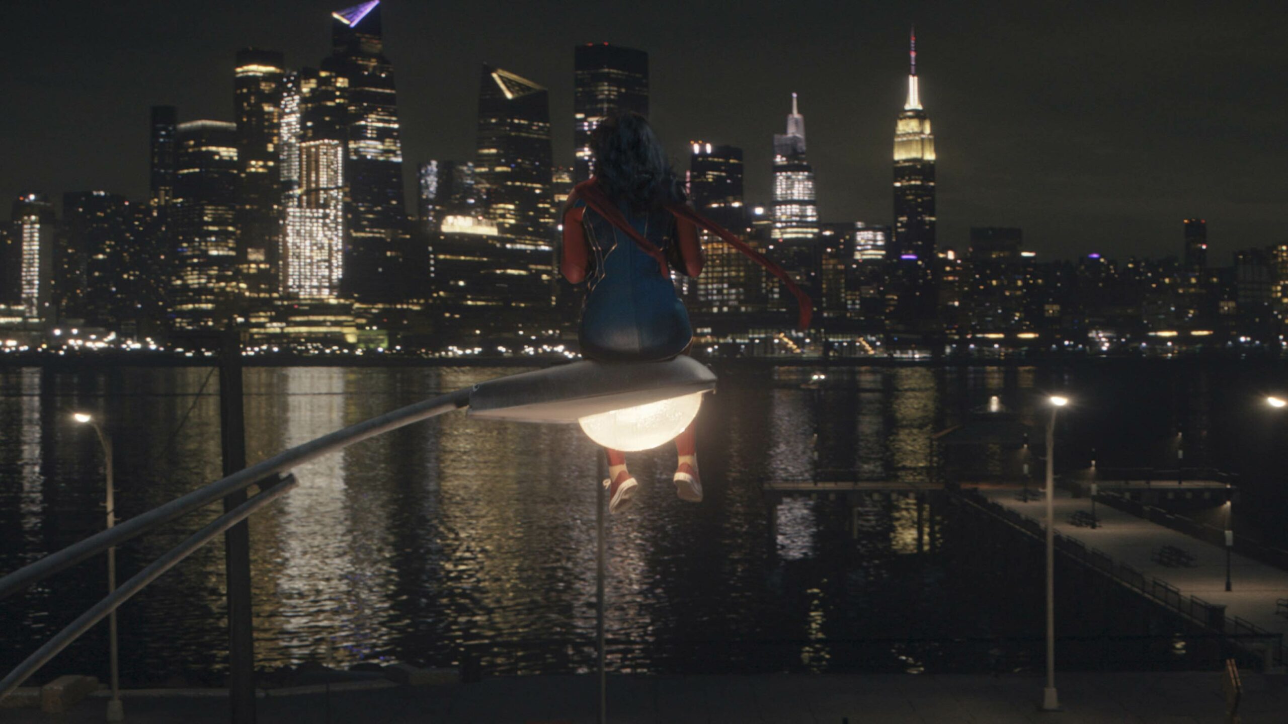 Ms. Marvel, played by Canada's Iman Vellani, sits on a lamppost and stares across a lake towards a distant city