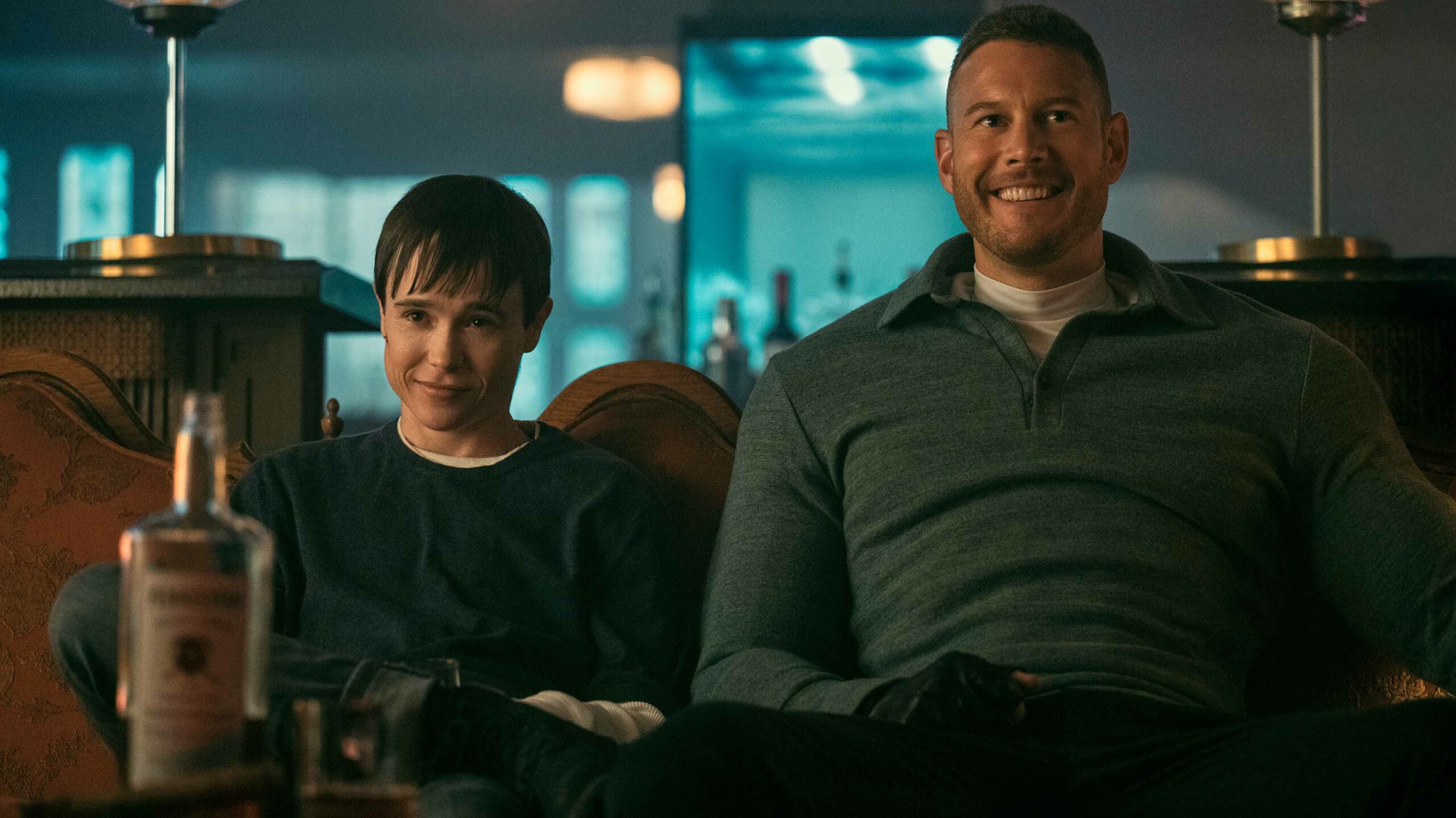 The Umbrella Academy. Elliot Page as Viktor and Tom Hopper as Luther are pictured. They are sitting on a coach looking happy.