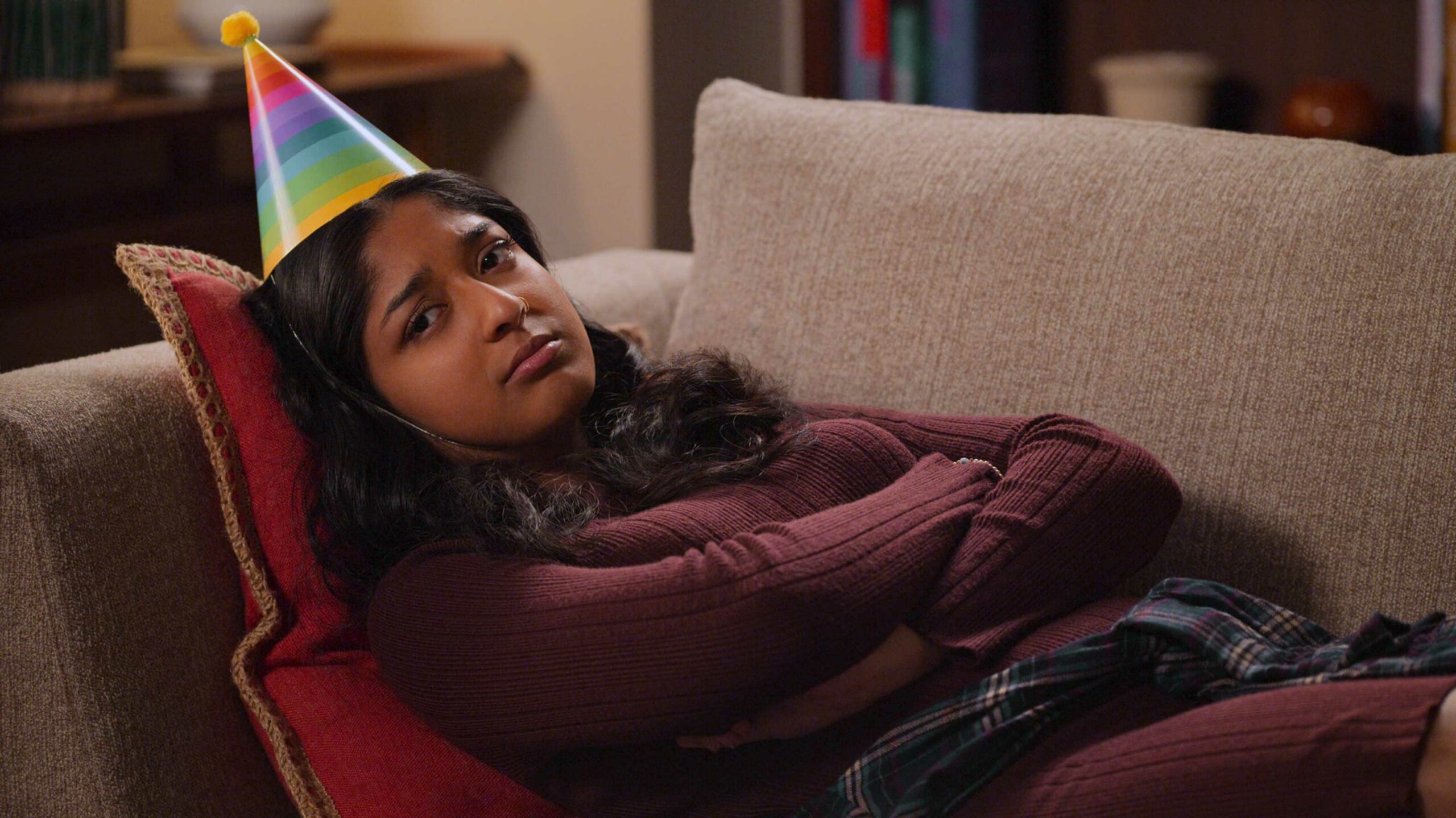 Never Have I Ever Season 3 Devi frowning on couch with birthday hat