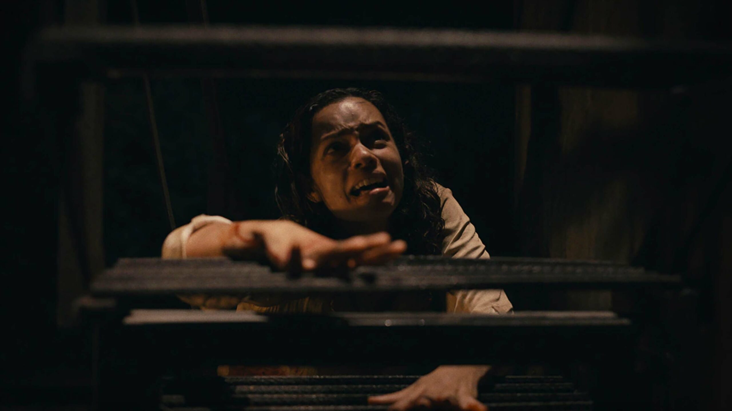 Tess, a young Black woman played by Georgina Campbell, in the 2022 horror movie Barbarian. She is crawling up stairs while crying.
