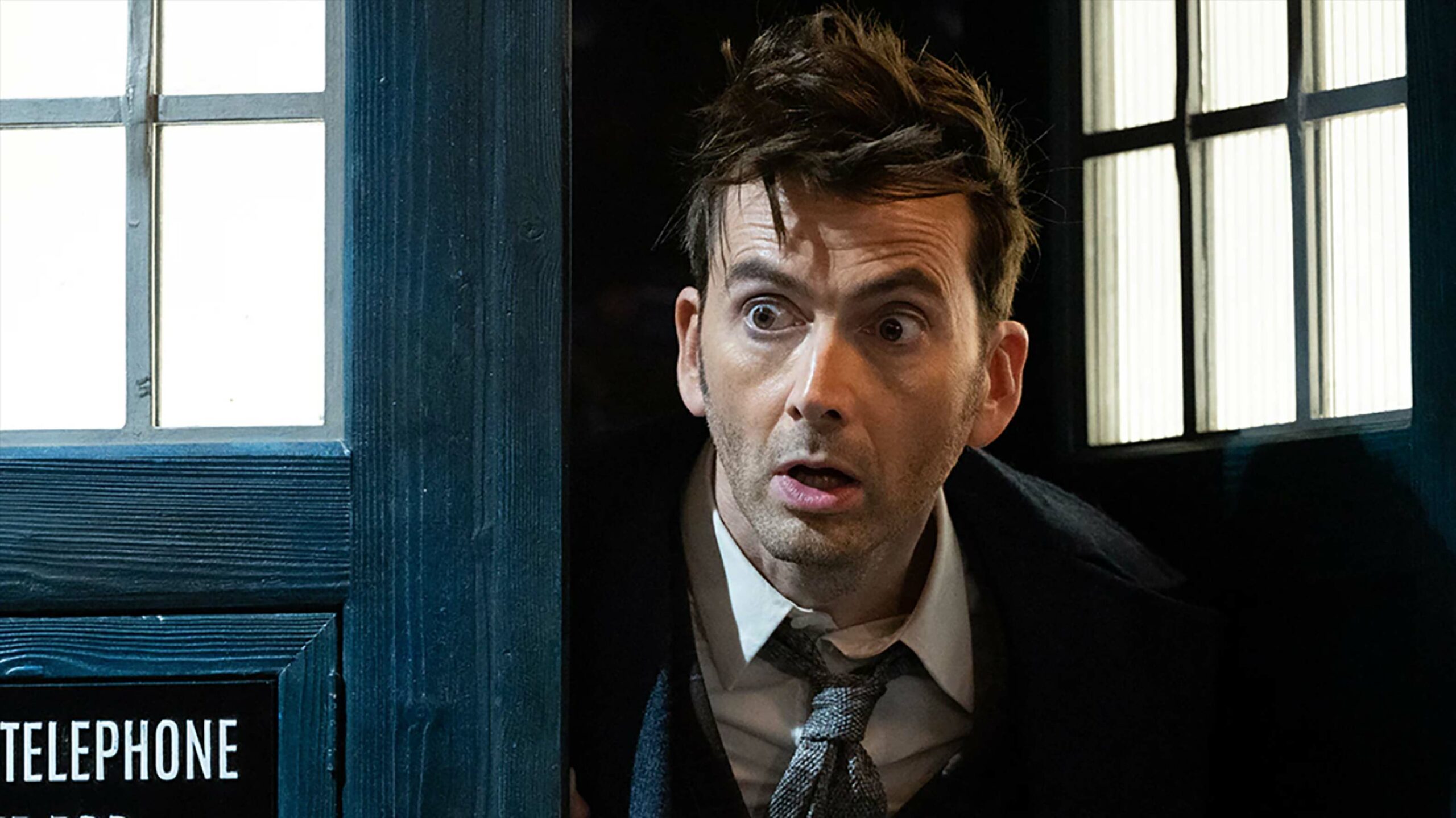 David Tennant as The Doctor in Doctor Who. He's looking out of a telephone box looking surprised.